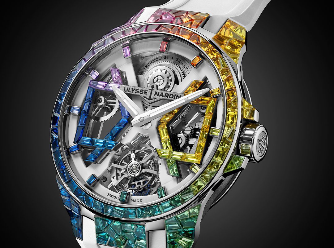 The Limited-Edition Ulysse Nardin Blast 'Sparkling Rainbow' features an exposed mechanical movement and a bezel adorned with multicolored gemstones, set on a chic white strap for true luxury flair.
