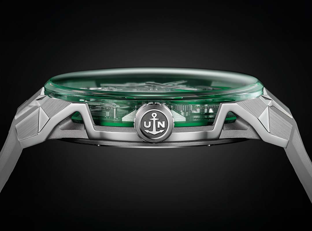 Side view of a luxury Ulysse Nardin wristwatch with a Silicon Green crystal face, visible internal components, and a crown featuring an anchor logo with the letters "U" and "N.