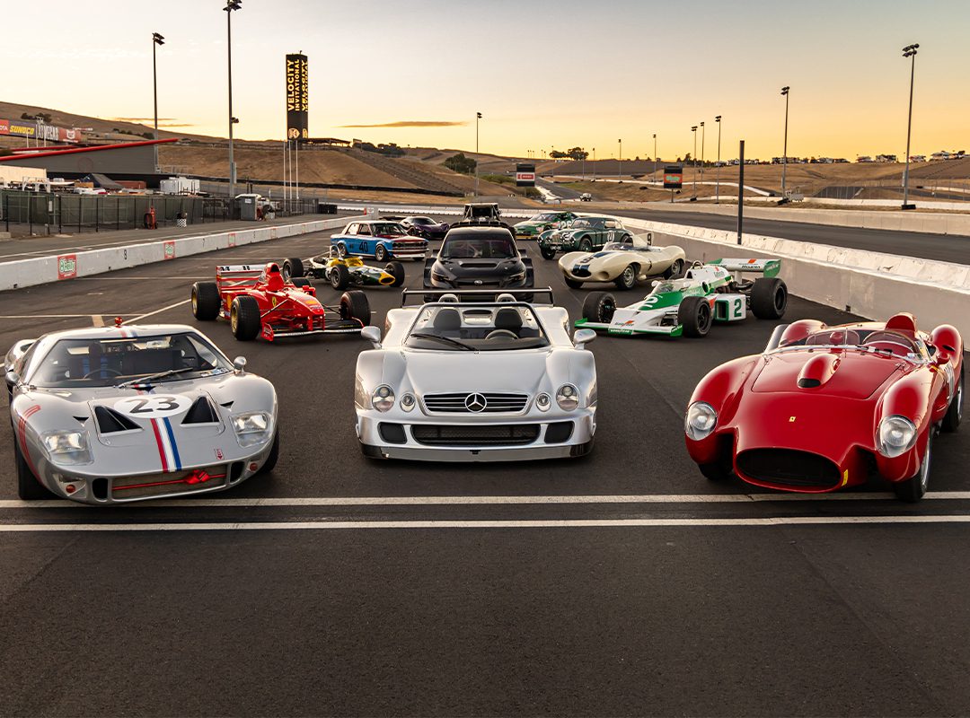 A stunning lineup of vintage and classic racing cars graces the track at sunset during the vibrant Motorsport Festival, showcasing an eclectic mix of styles and colors.