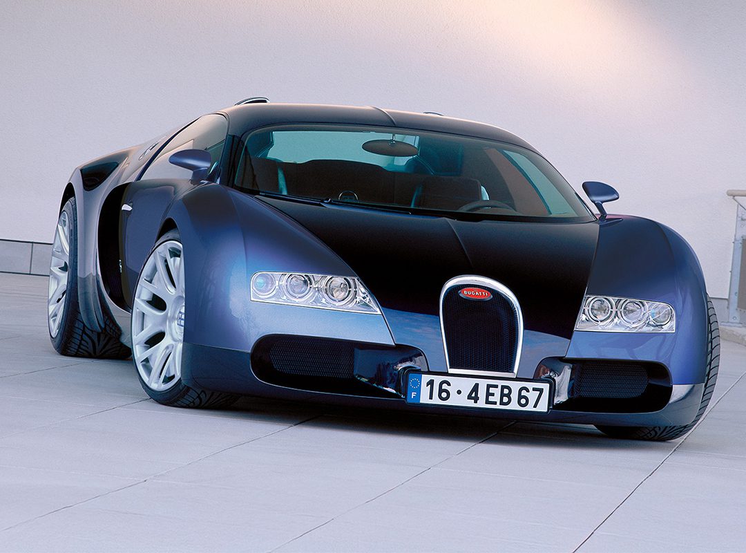 A blue and black Bugatti Veyron hypercar is parked on a tiled surface in front of a plain light-colored wall.