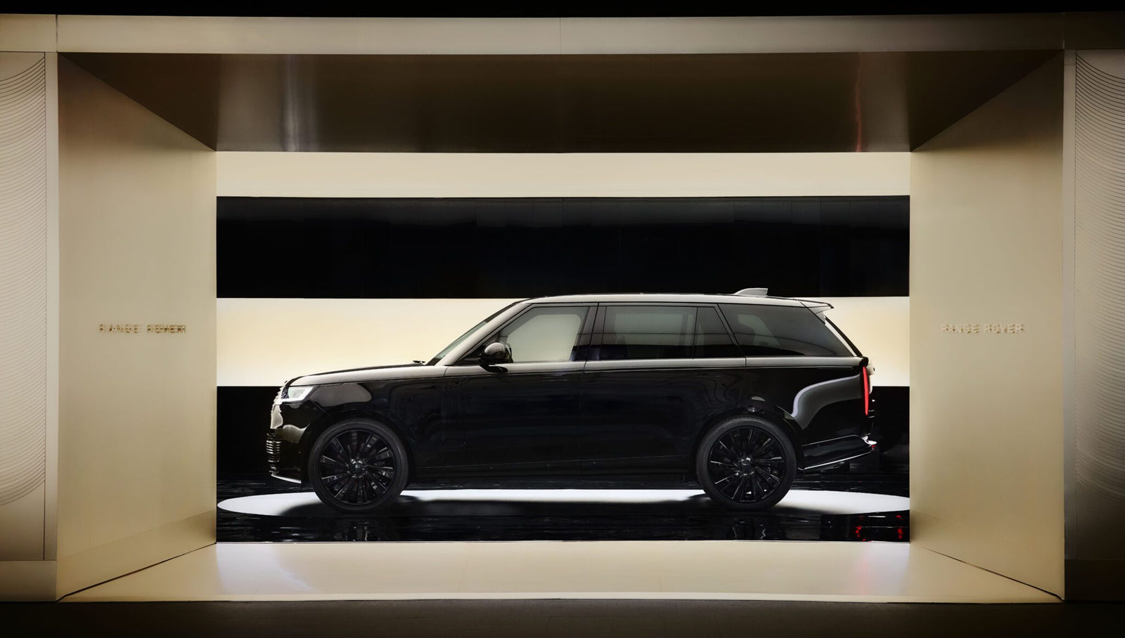 A black Range Rover SUV is displayed in a minimalist, light-colored showroom with bright horizontal light panels.