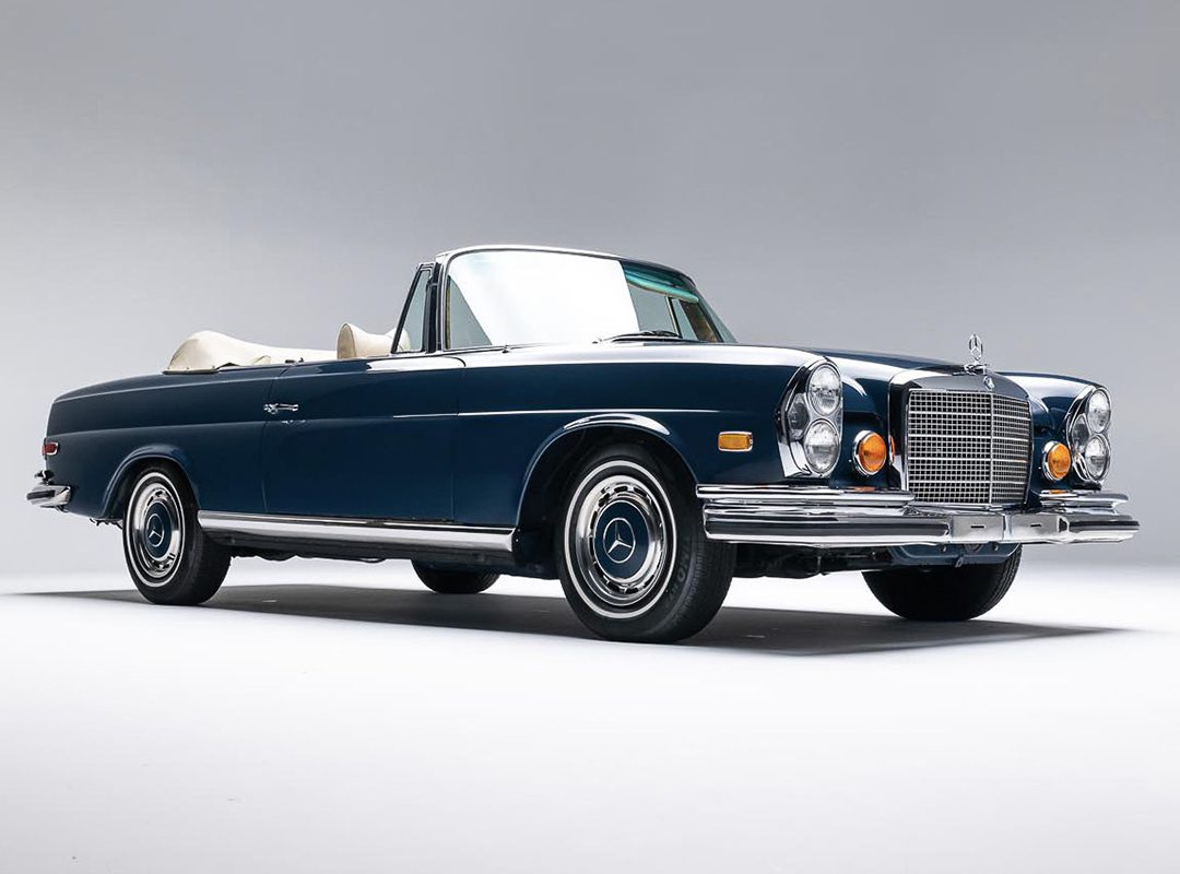 A classic dark blue convertible car with chrome accents and a beige interior, photographed in a studio setting against a plain gray background, ready to shine at the Auburn Auction by Worldwide Auctioneers.