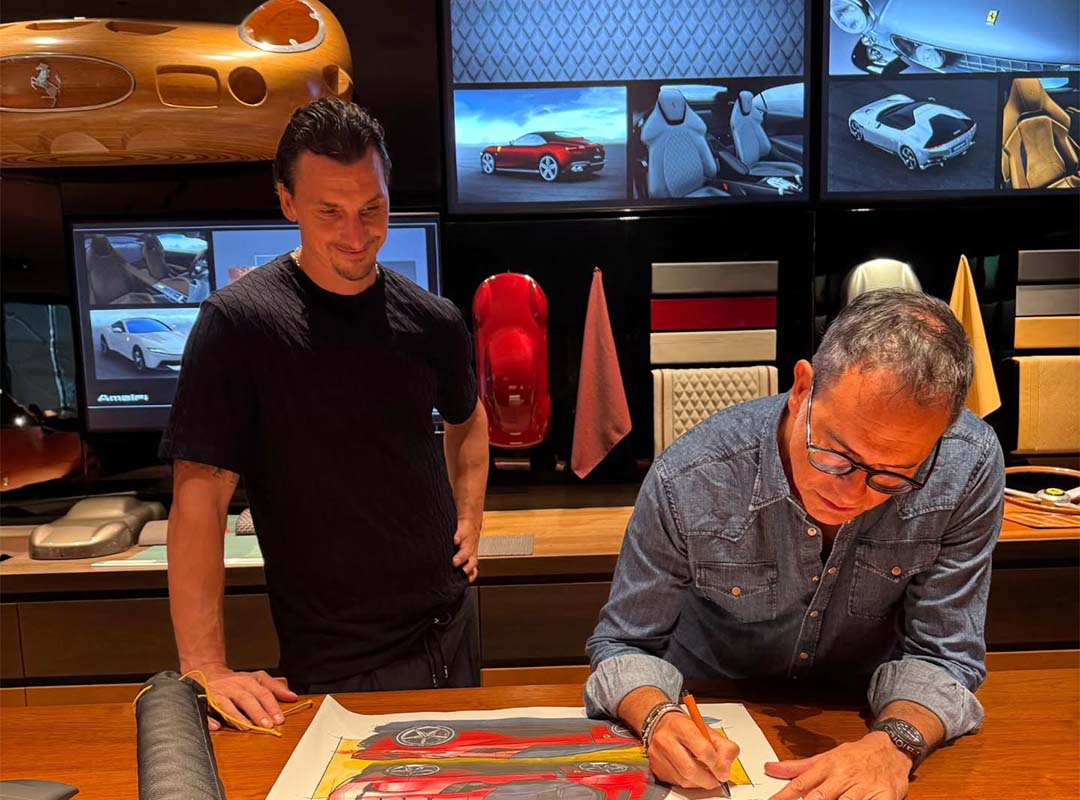 Two men are in a design studio; one sketches a car on paper while the other observes. Behind them, images of the Ferrari F80 and materials are displayed—echoing the creative spirit of Flavio Manzoni.