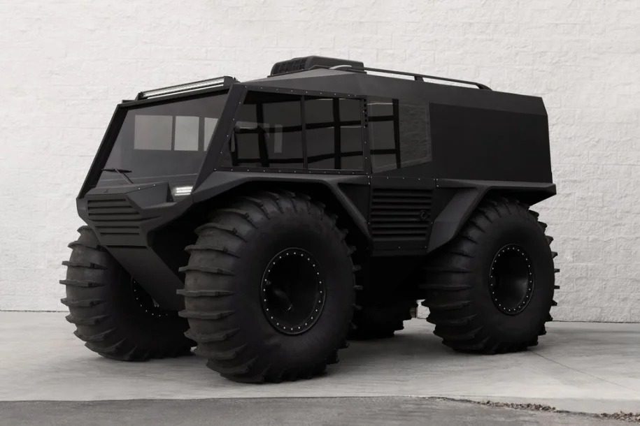An amphibious, matte black Atlas ATV with oversized tires is parked on a concrete surface in front of a white brick wall—an impressive off-road vehicle for sale.