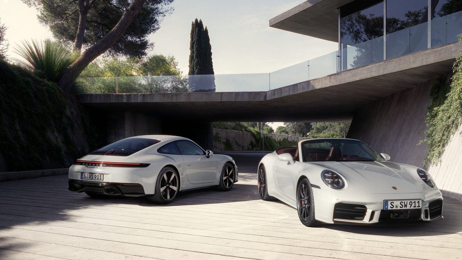 Two white sports cars parked outdoors on a sunny day, near a modern building with large windows and surrounded by trees.