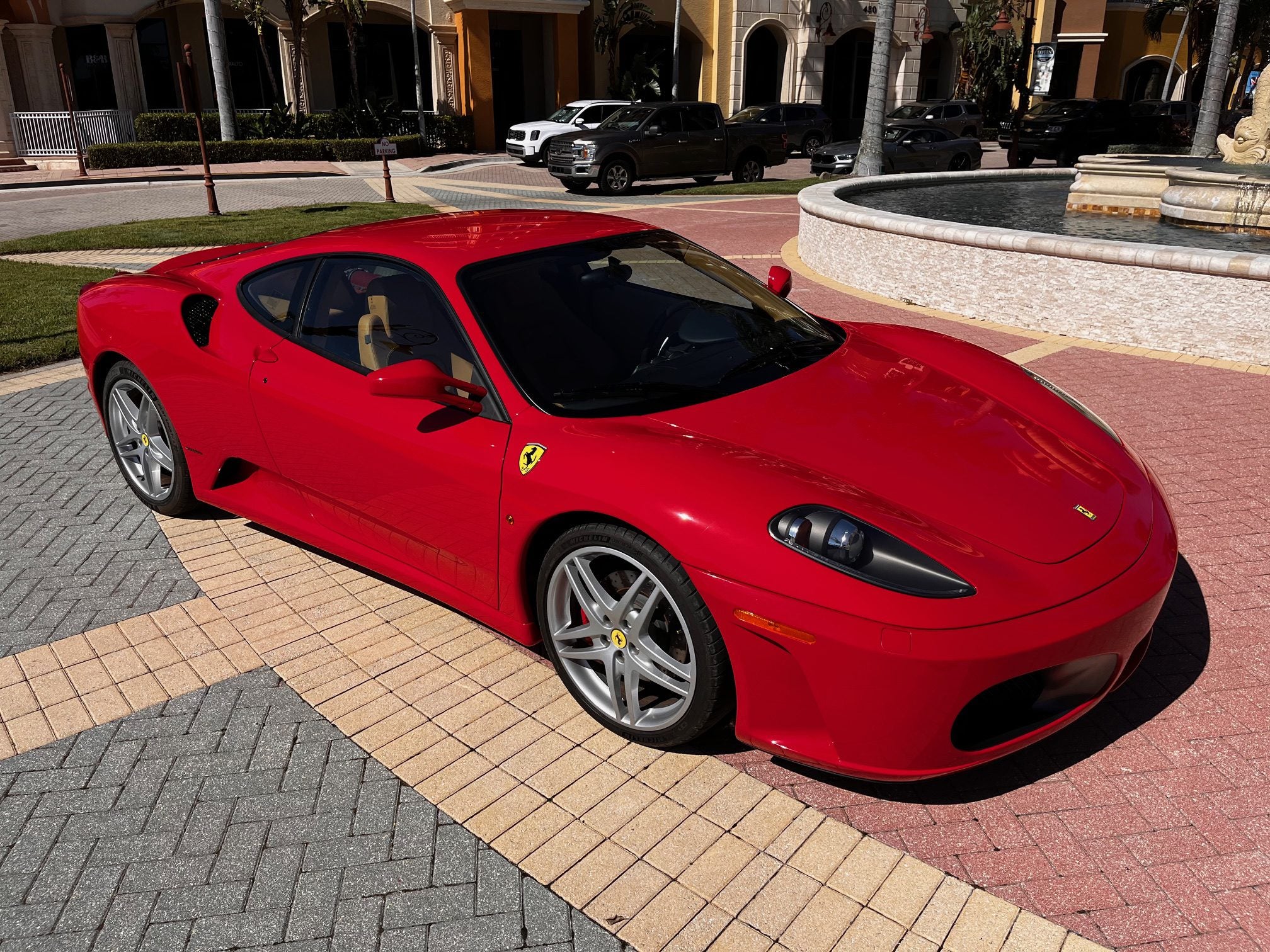 A sleek 2007 Ferrari F430 sits regally on the patterned pavement, framed by elegant buildings and a shimmering fountain, exuding an air of presidential provenance.