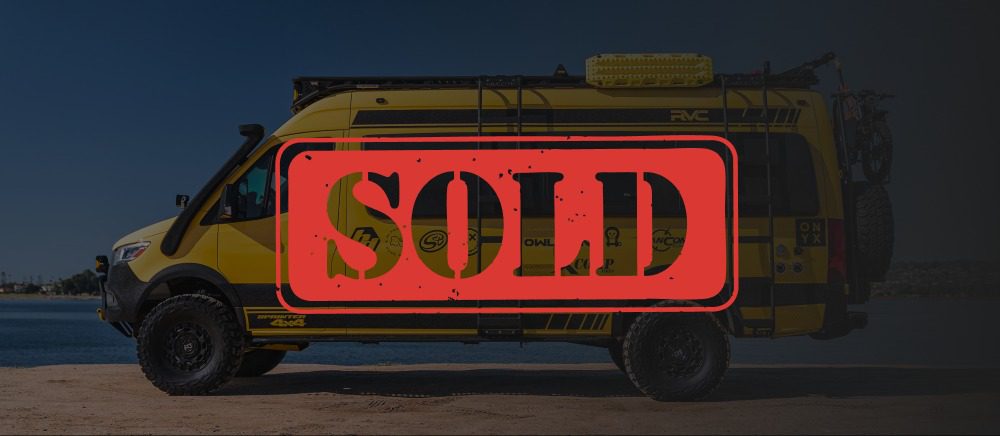 Yellow RC-1 off-road van parked by water, with a large red "SOLD" stamp overlay. Another adventure-ready vehicle from Rogue Van Company.