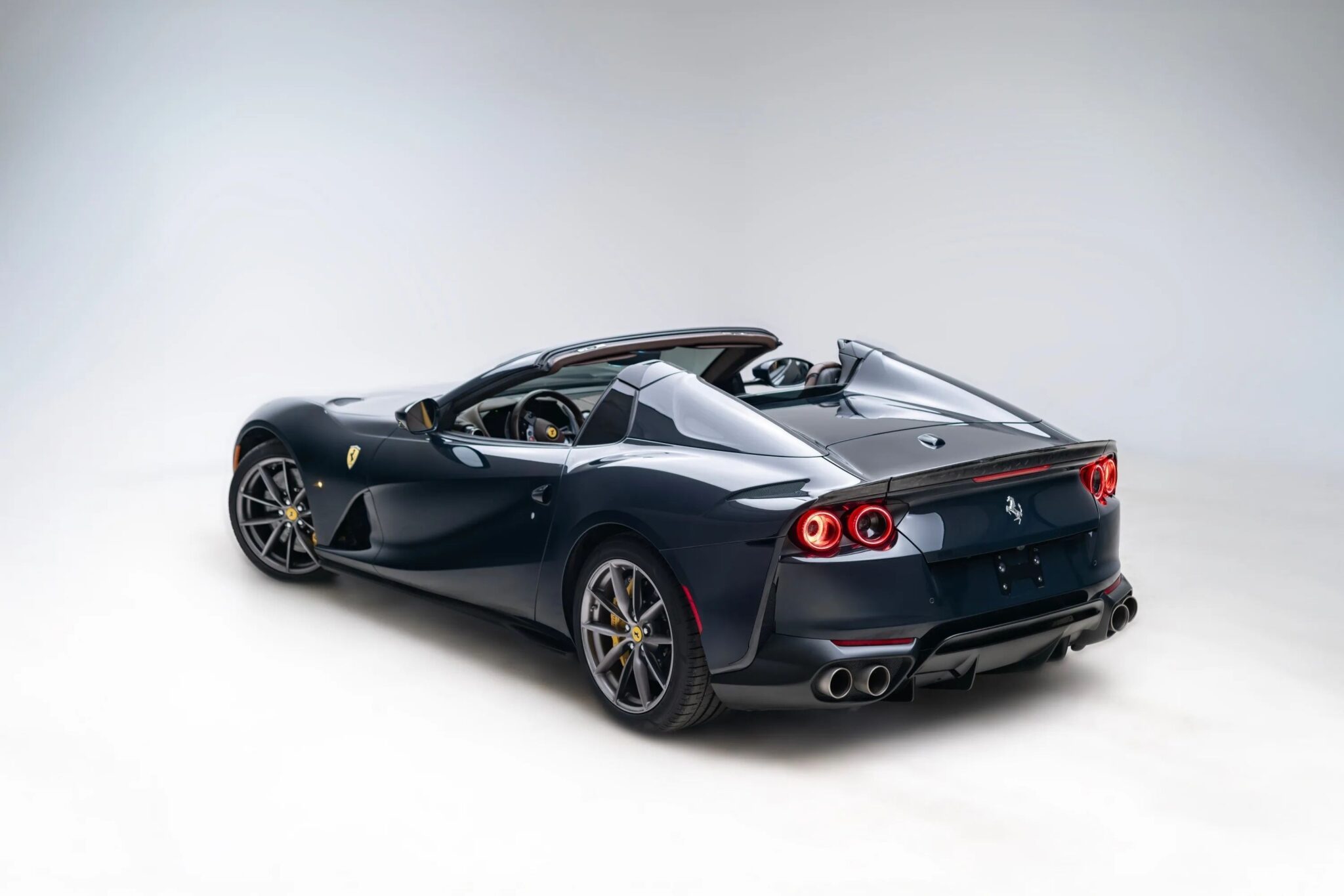 A dark blue Ferrari convertible sports car is shown in a studio with its roof down, viewed from the rear three-quarter angle.