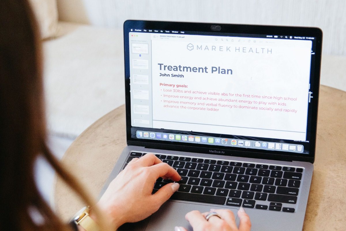 Person typing on a MacBook displaying a slide titled "Treatment Plan" with primary goals for a personalized health upgrade and improved energy.