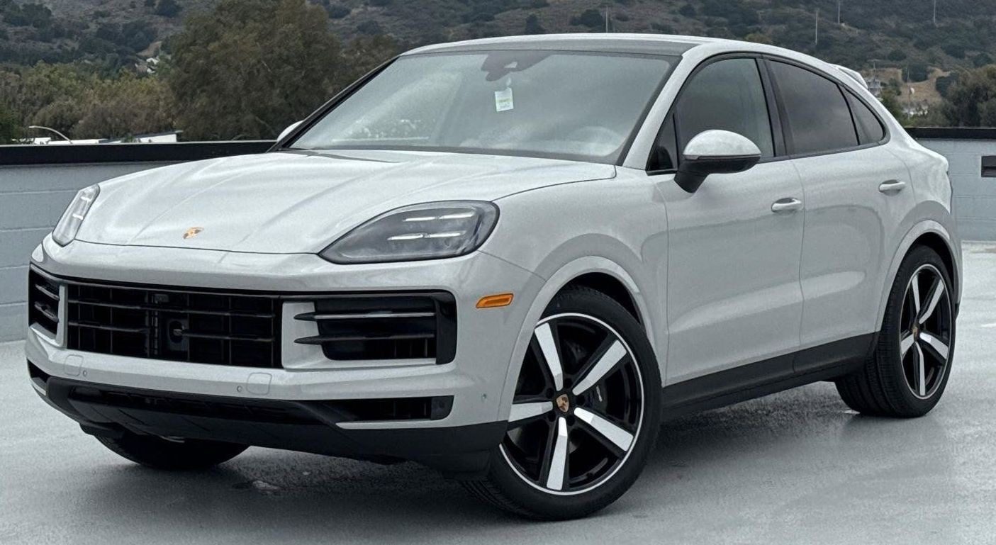 A white Porsche SUV, available through the best car lease offers, is parked outdoors on a concrete surface with hills and trees in the background.