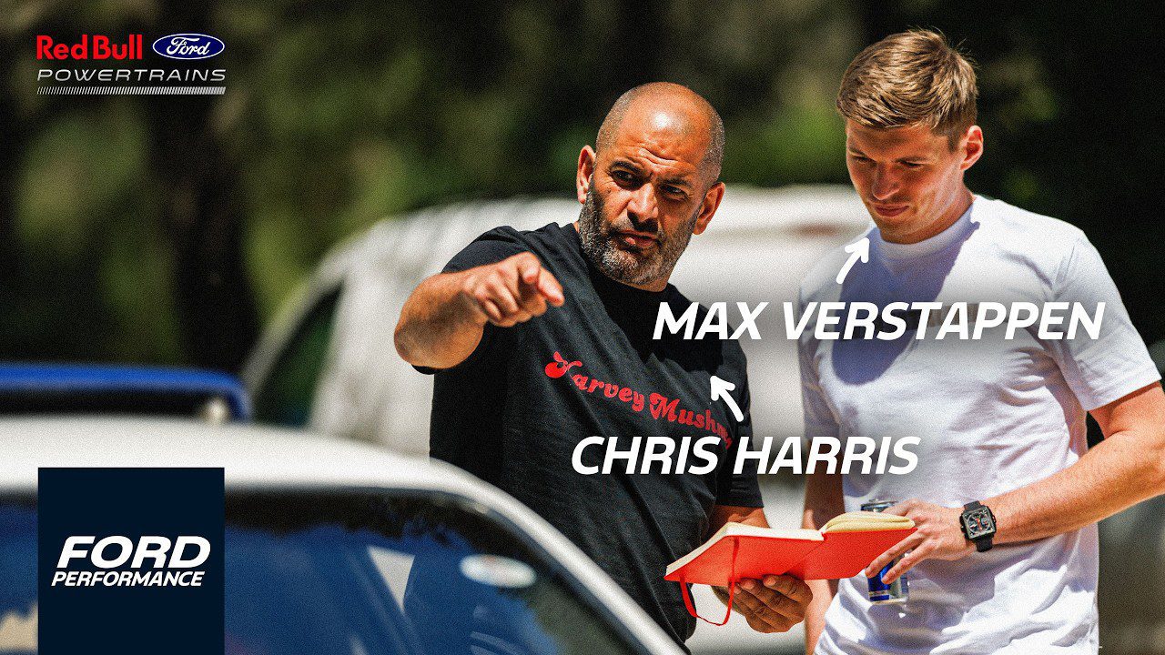 Chris Harris and Max Verstappen stand outdoors beside a Ford Mustang GTD; one points ahead while the other holds a red box. Text labels identify them, with Ford and Red Bull logos visible in the background.