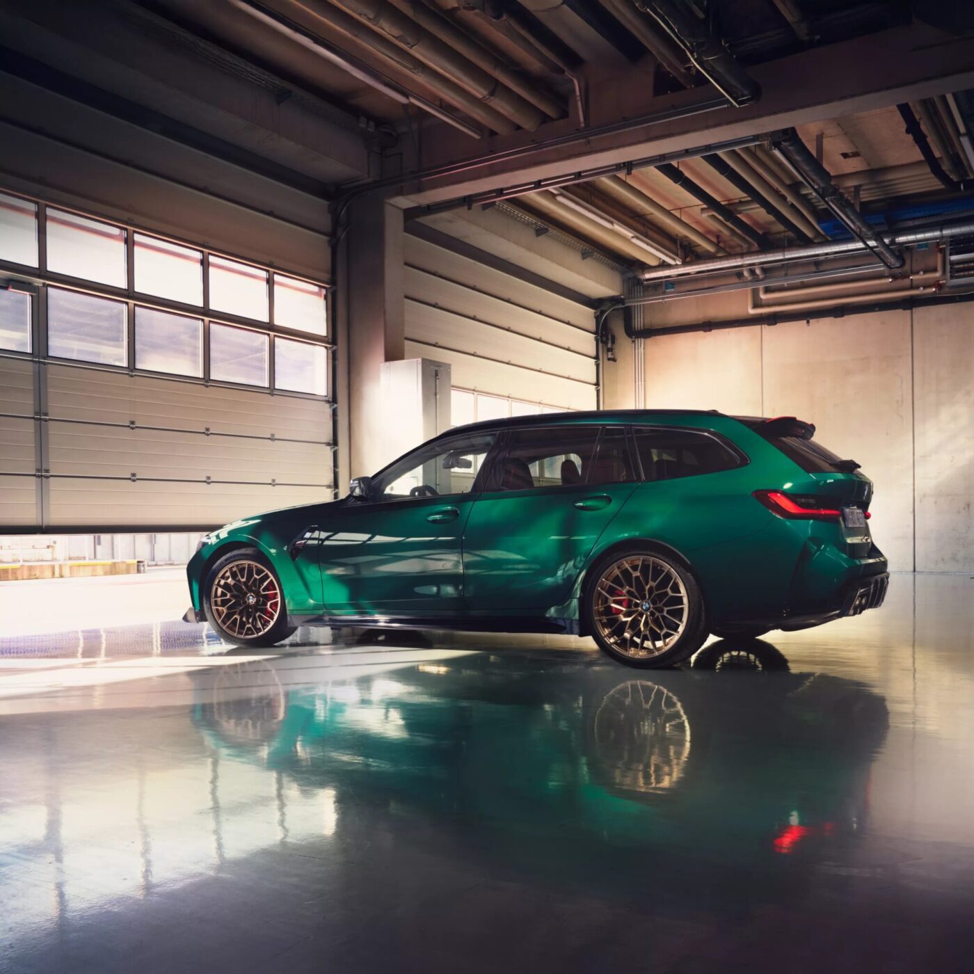 A sleek green BMW sports wagon is parked in an industrial-style garage with polished concrete floors and large windows, showcasing the brand's commitment to EV growth as it gears up for Q1 2025 sales.