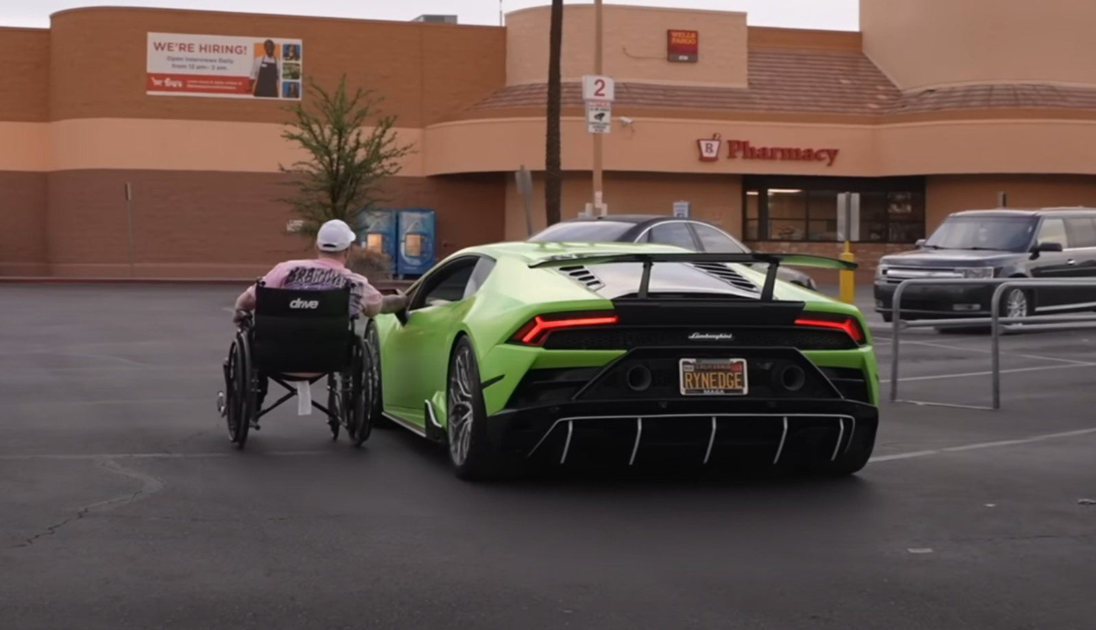 Garet Thomas, in a wheelchair, moves toward a green Lamborghini parked in a pharmacy lot during Monterey Car Week 2025. A "We're Hiring" sign is visible on the building in the background.