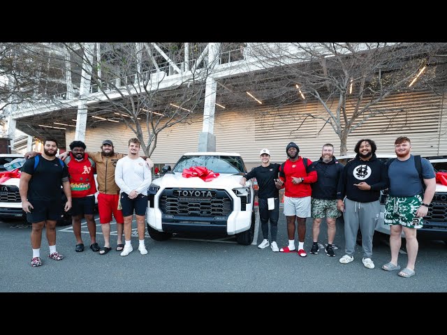 A group of nine people, including NFL QB Brock Purdy, stand proudly in front of a row of white Toyota TRD Pros with red bows on the hoods, posing for a photo outdoors.