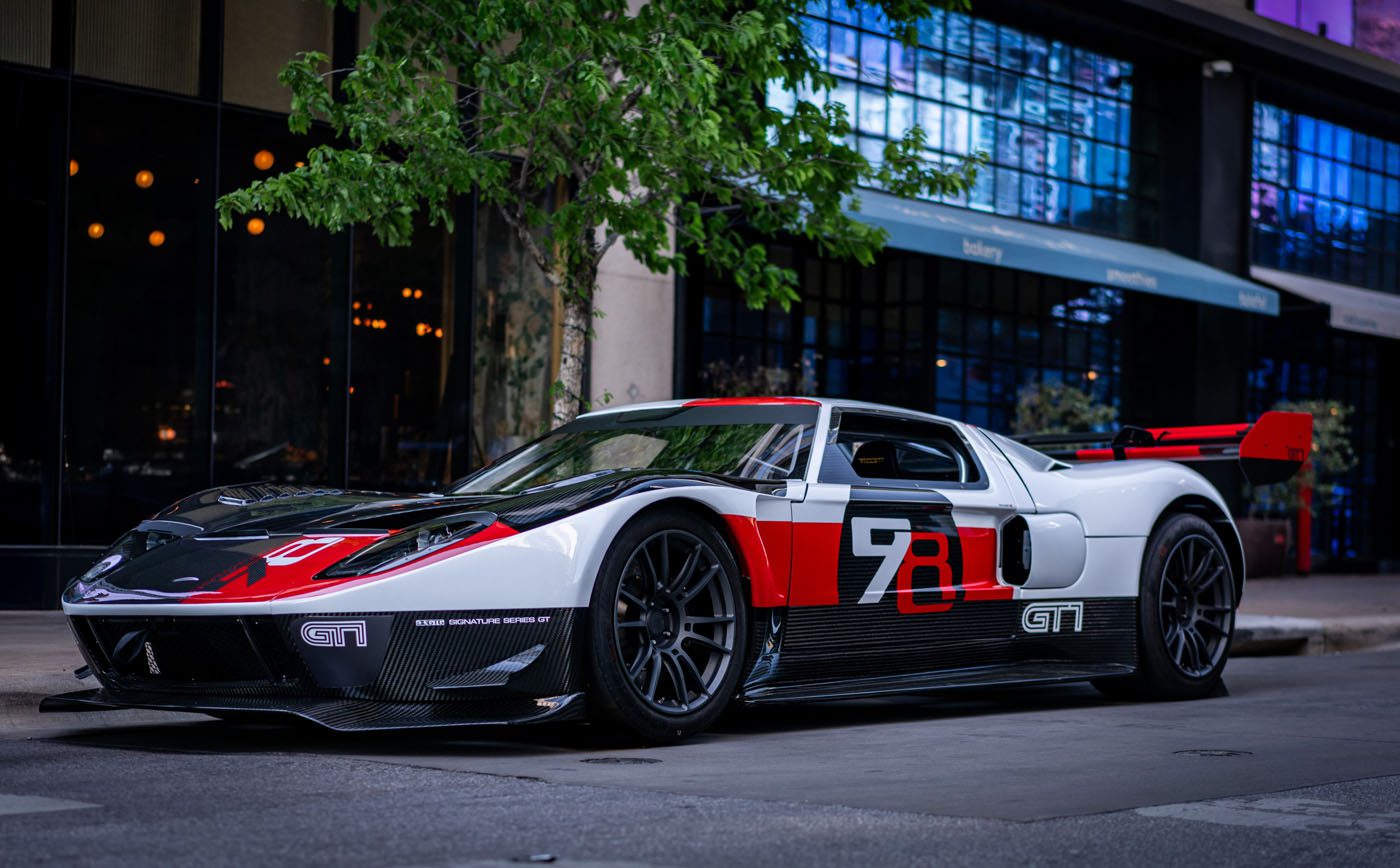 A sleek black and white Ford GT with red accents and the number "78" graces a city street, reflecting the urban architecture around it. Enhanced by Graham Rahal Performance, this LYNX Motors masterpiece stands poised next to a leafy tree.