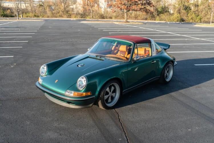 A green vintage Porsche 911 Targa, customized by Singer with a red roof and tan interior, is parked in an empty lot—a true duPont REGISTRY classic.