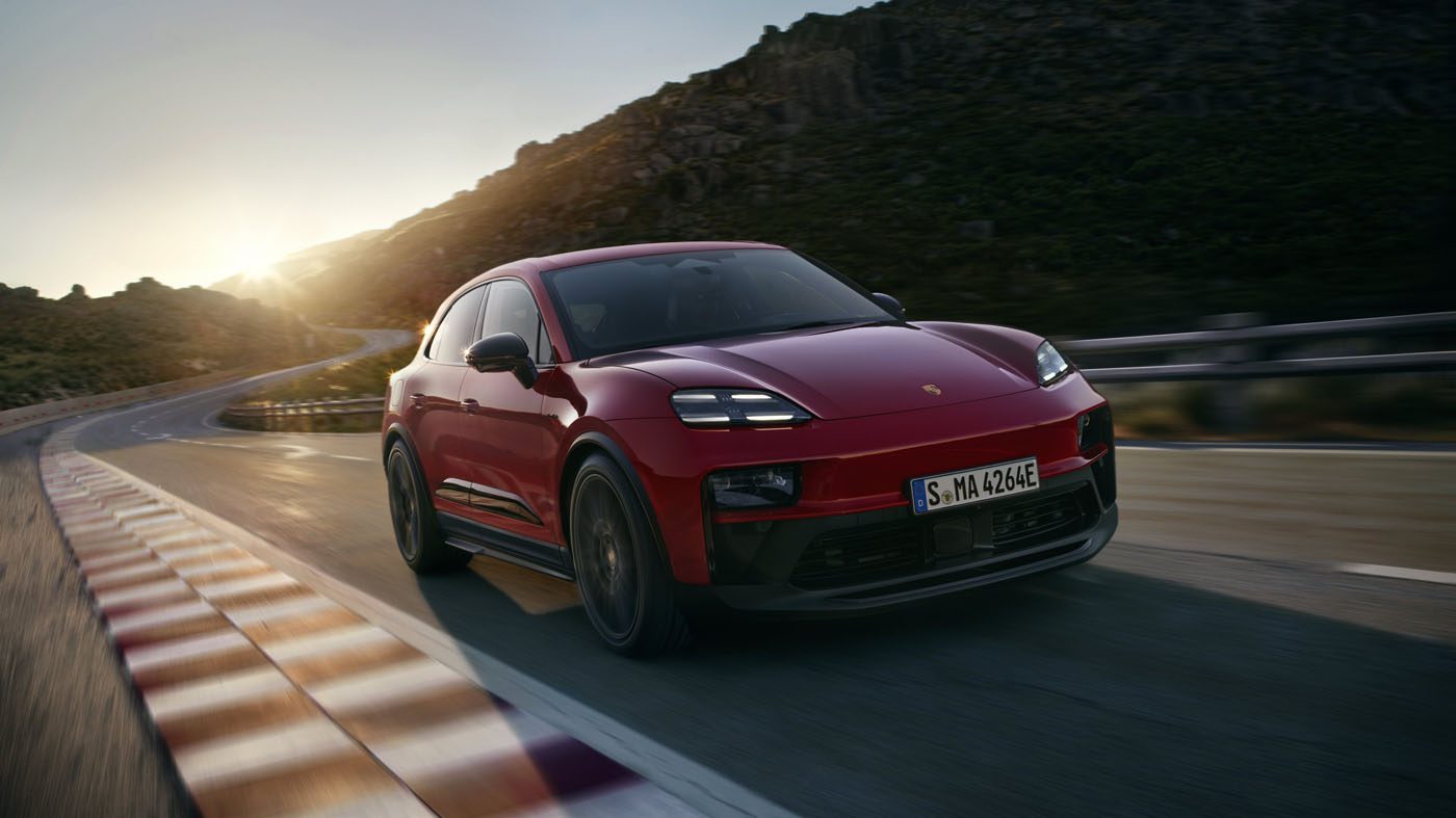 A red 2026 Macan Electric GTS SUV drives on a winding mountain road at sunset, with rocky hills in the background.