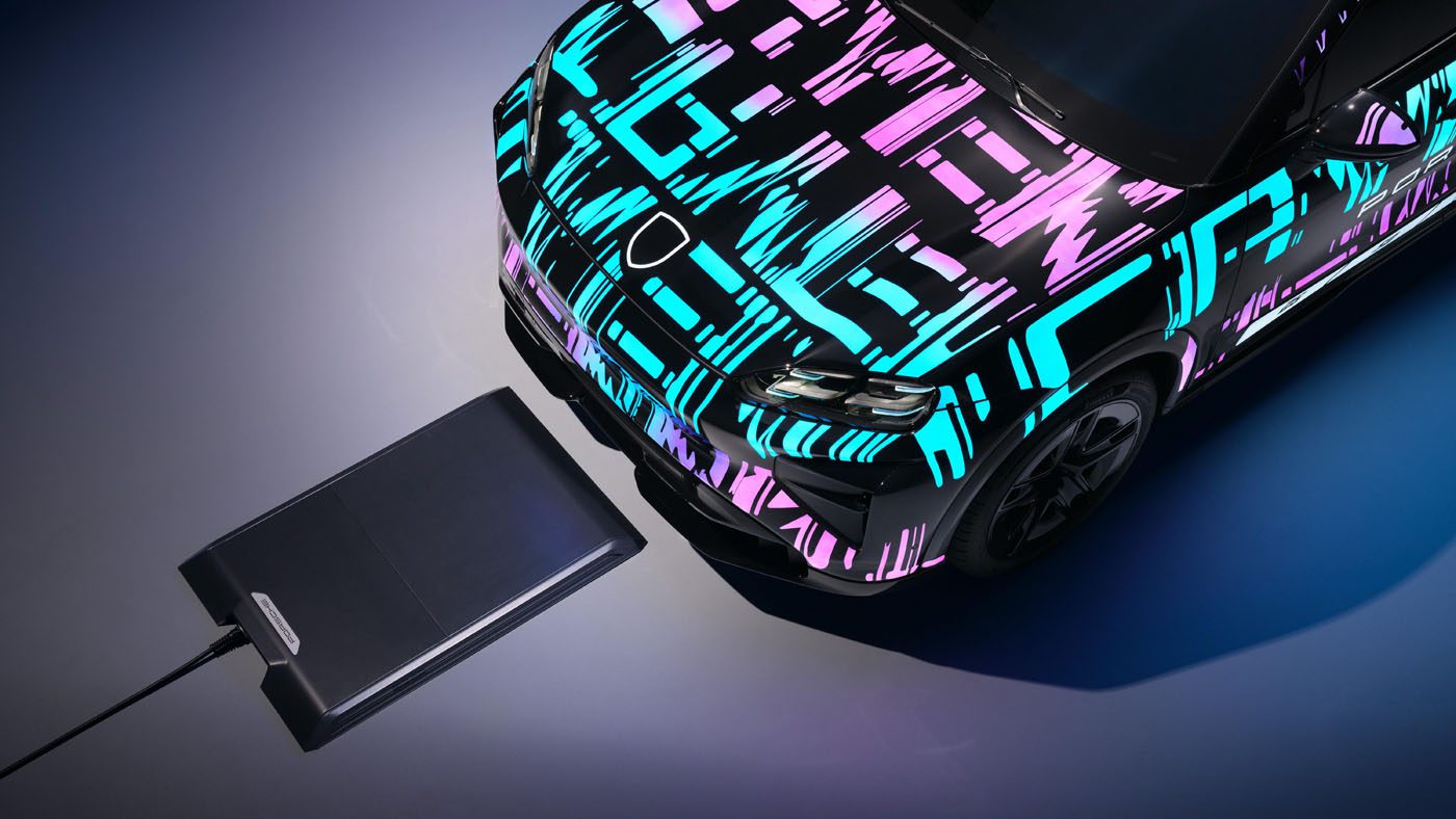 A Porsche Cayenne Electric with a colorful geometric wrap is positioned above a wireless charging pad, demonstrating how it works as an advanced electric vehicle charging system.