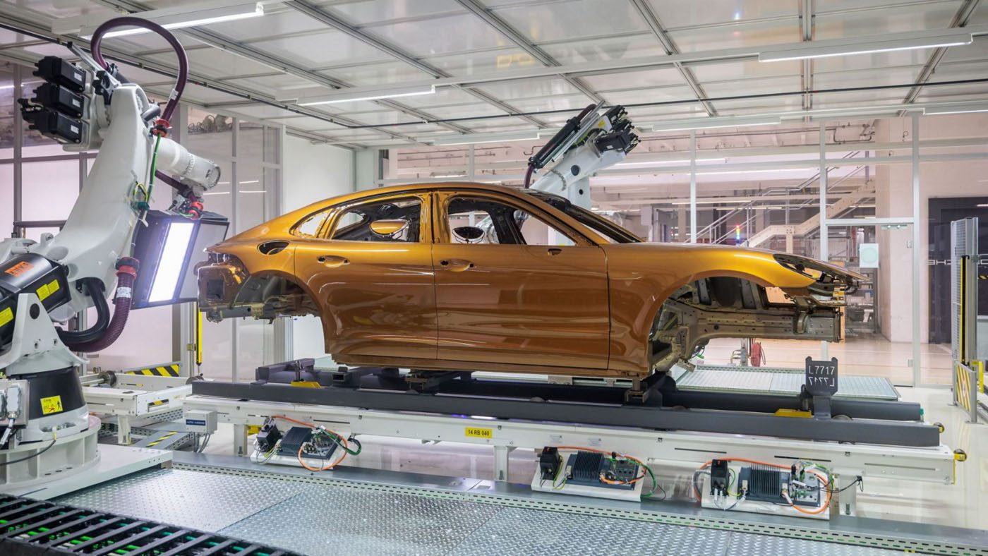Robotic arms, guided by AI, skillfully assemble a brown car frame on the production line of a modern factory setting, preparing it for the meticulous Porsche paint process.