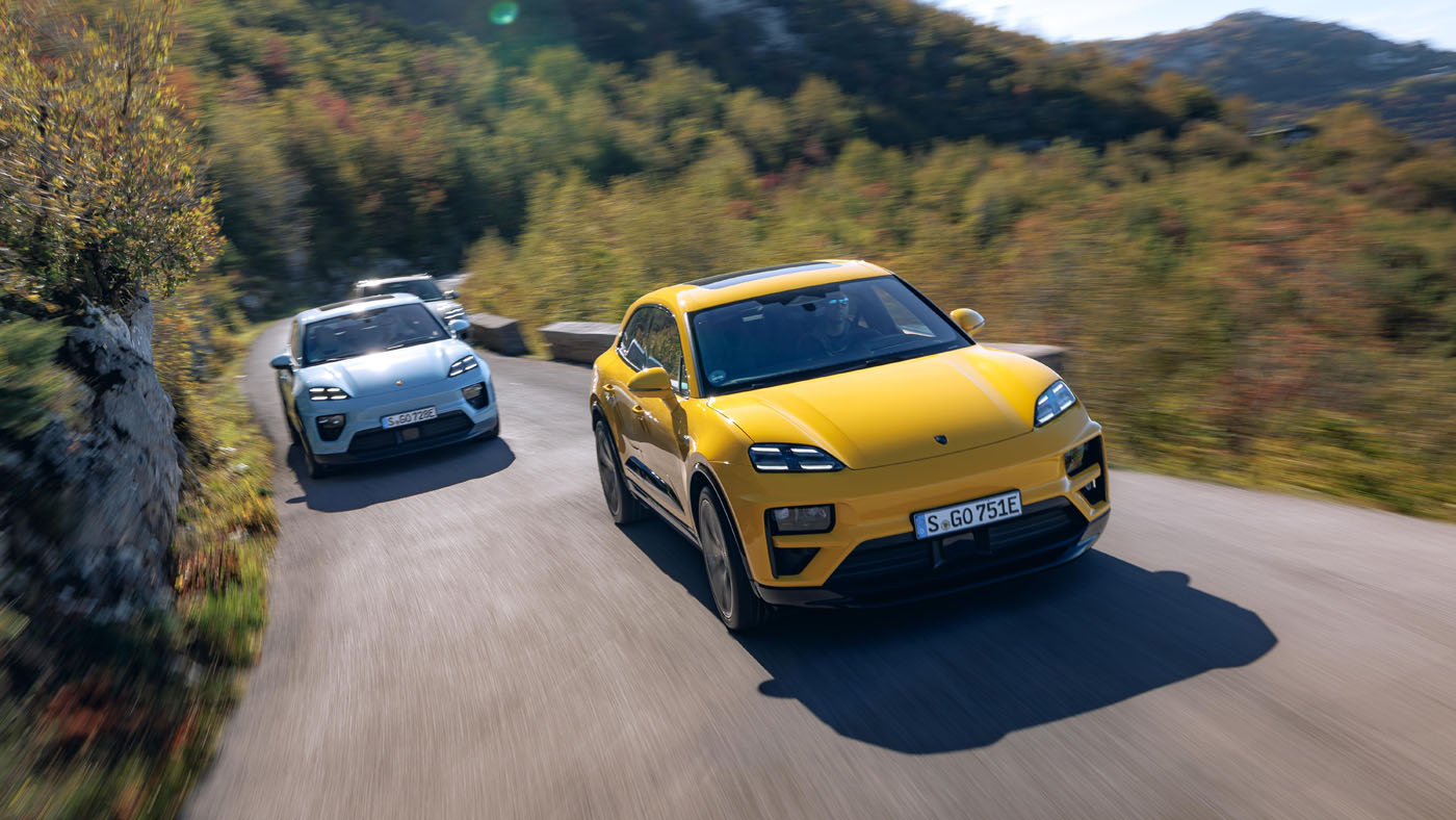 A yellow Macan Turbo Electric leads a silver car on one of Europe's best driving roads. The winding mountain route is framed by blurred greenery and hills beneath a clear sky, perfect for enjoying the Porsche experience.