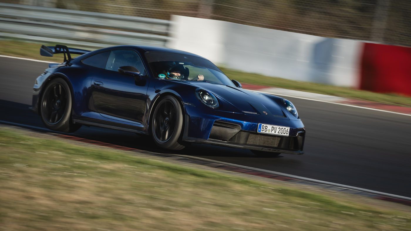 A dark blue Porsche 911 GT3, the fastest manual production car, speeds along a racetrack, with a blurred background hinting at its Nürburgring record-breaking motion.