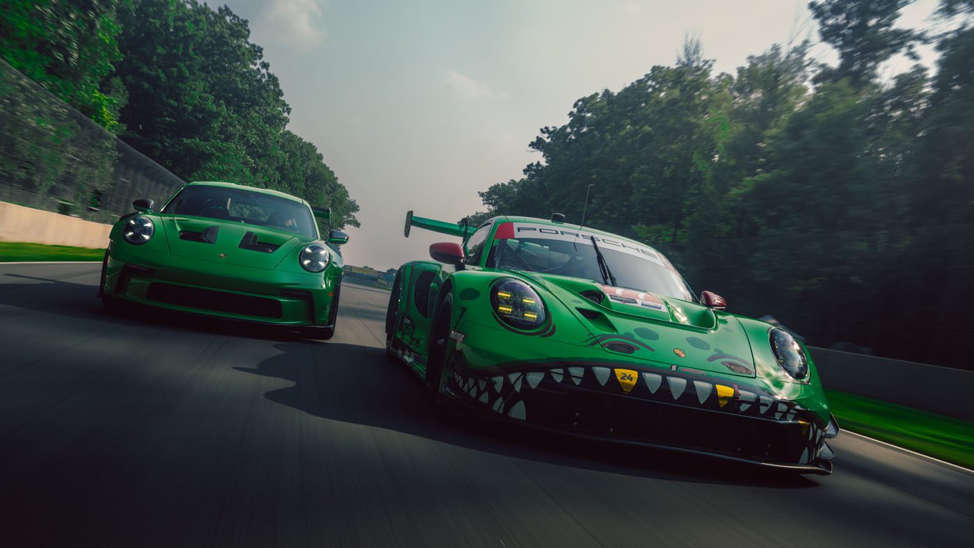 Two green Porsche cars—a Rexy race car and a Porsche 911 GT3 RS Sonderwunsch edition—drive side by side on a racetrack surrounded by trees.