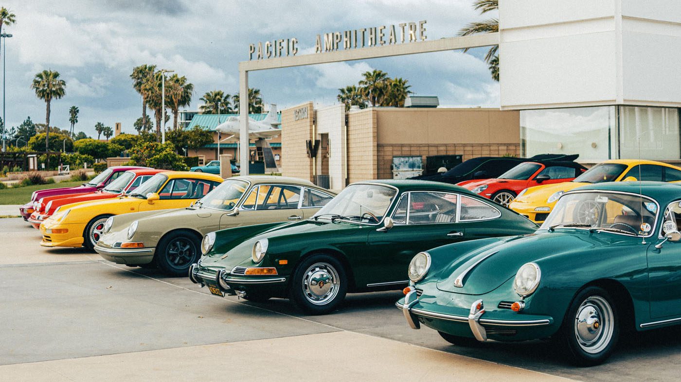 A row of vintage and classic cars, including Porsche models, parked in front of a building with a "Pacific Amphitheatre" sign on a cloudy day during the 2025 Air|Water Event.