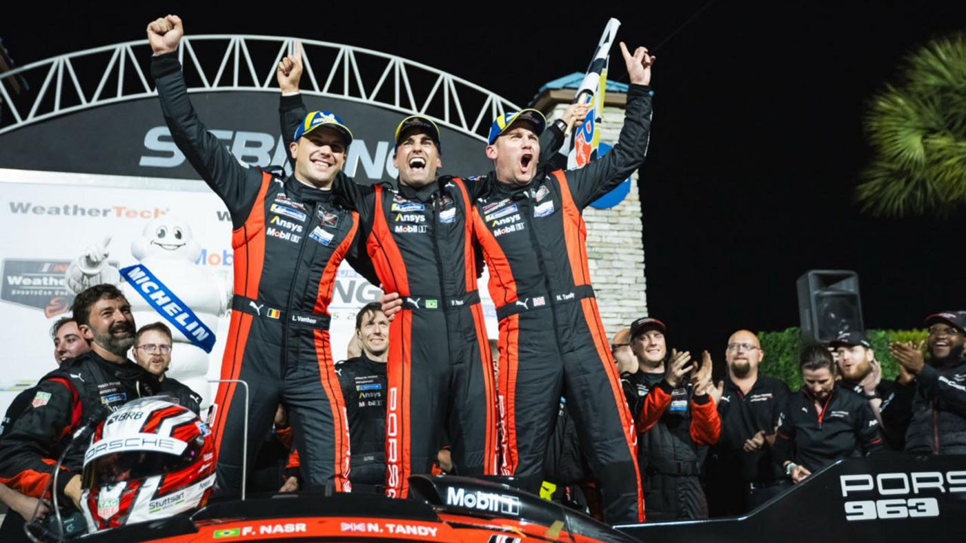Three race car drivers in matching suits celebrate their Porsche victory on the podium, arms raised high. The iconic race car and cheering team members form a jubilant backdrop after the intense 12 Hours of Sebring spectacle.