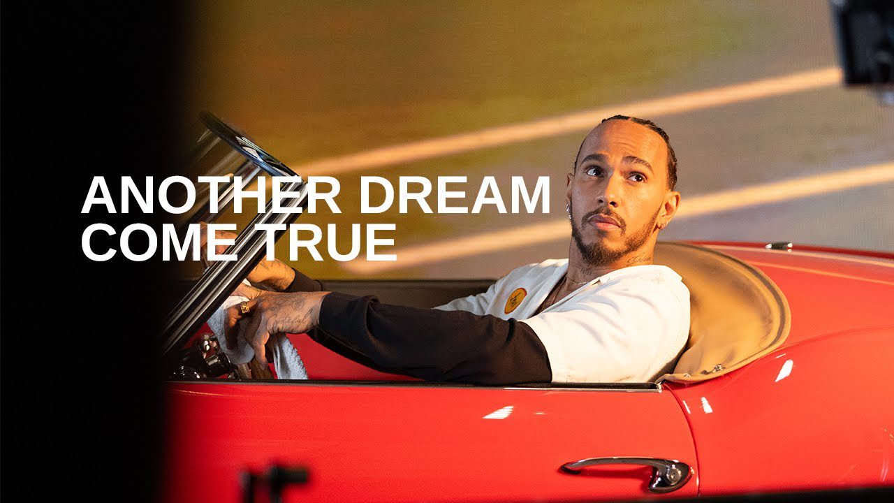 Person sitting in a red car, looking upward. Large text reads: "Another Dream Come True." It's like their own Ferris Bueller's Day Off moment or channeling Lewis Hamilton on the track.