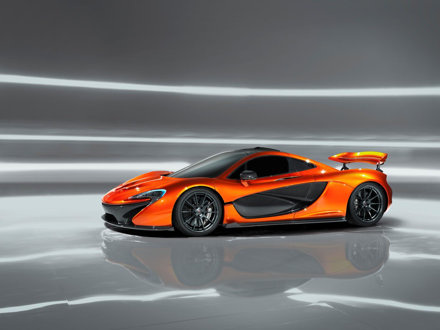 A sleek, orange McLaren P1 sports car with a prominent rear spoiler is showcased against a reflective gray background.