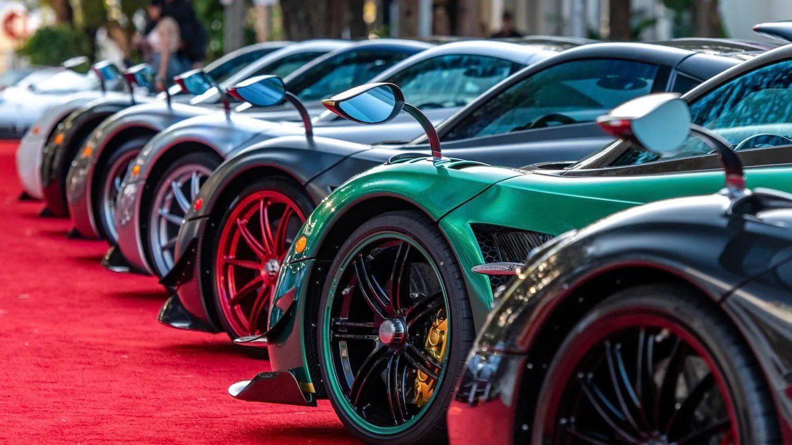 A line of luxury sports cars, dynamic 2024 models, parked on a red carpet, showcasing various colors and sleek designs.