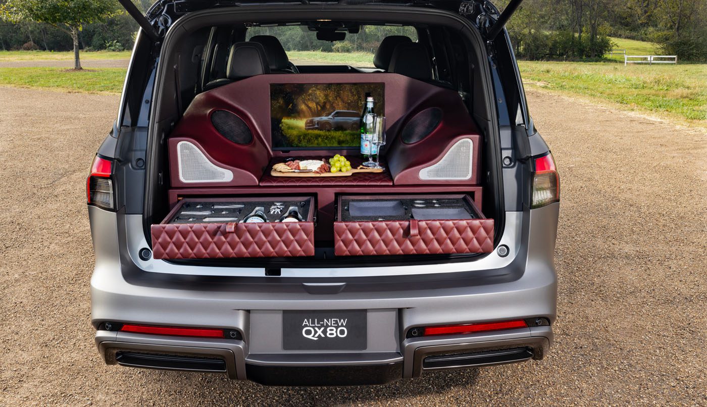 The Infiniti car trunk transforms into a Tailgating Luxury experience, featuring padded shelves, a screen, and an array of beverages and snacks on display, mimicking an AUTOGRAPH Lounge Concept.