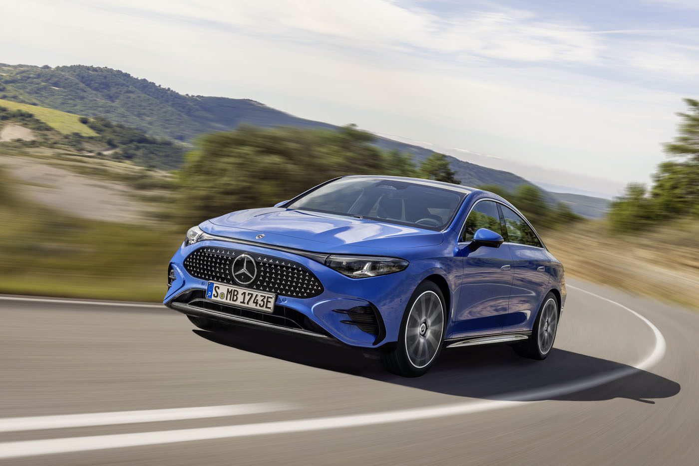 A blue Mercedes-Benz CLA sedan cruising along a rural road, surrounded by lush greenery and rolling hills, showcasing its groundbreaking tech in style.
