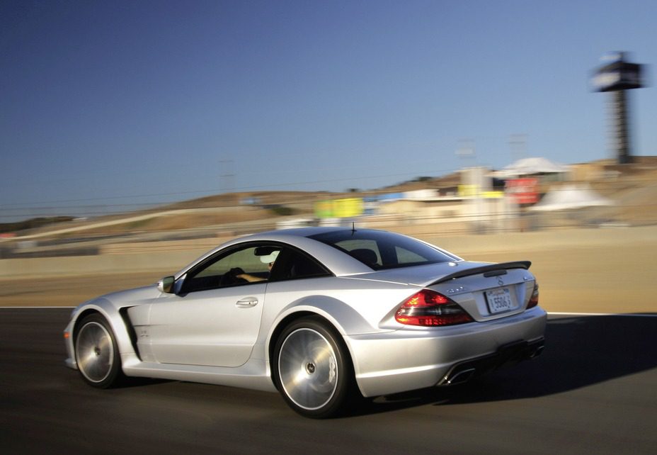 A silver sports car drives on a racetrack, with blurred background indicating motion and a clear sky above.