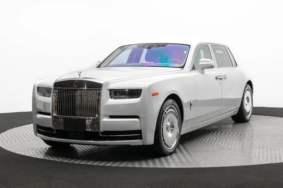 A silver Rolls-Royce Phantom Platino luxury sedan on display in a studio, featuring a prominent grille and sleek design.