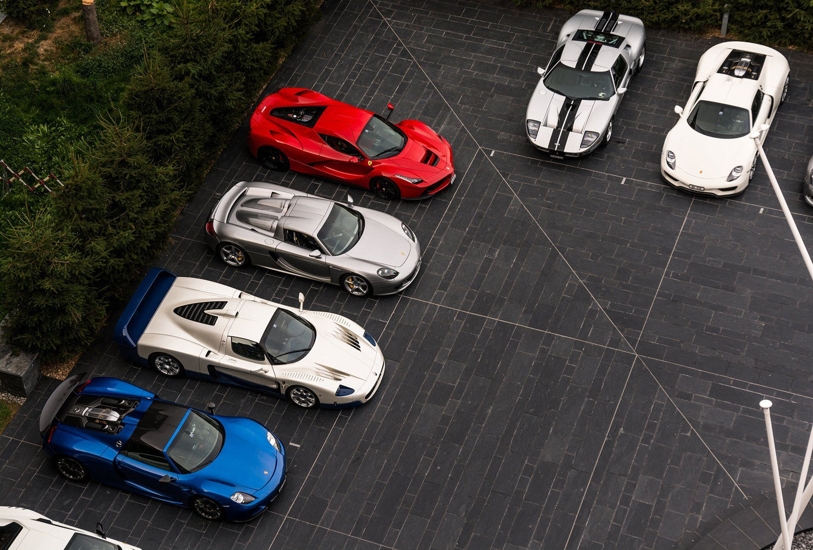 Six luxury sports cars, in blue, silver, red, and white, are parked in two parallel rows on a dark tiled driveway—an impressive lineup sure to captivate luxury car buyers and enthusiasts alike.