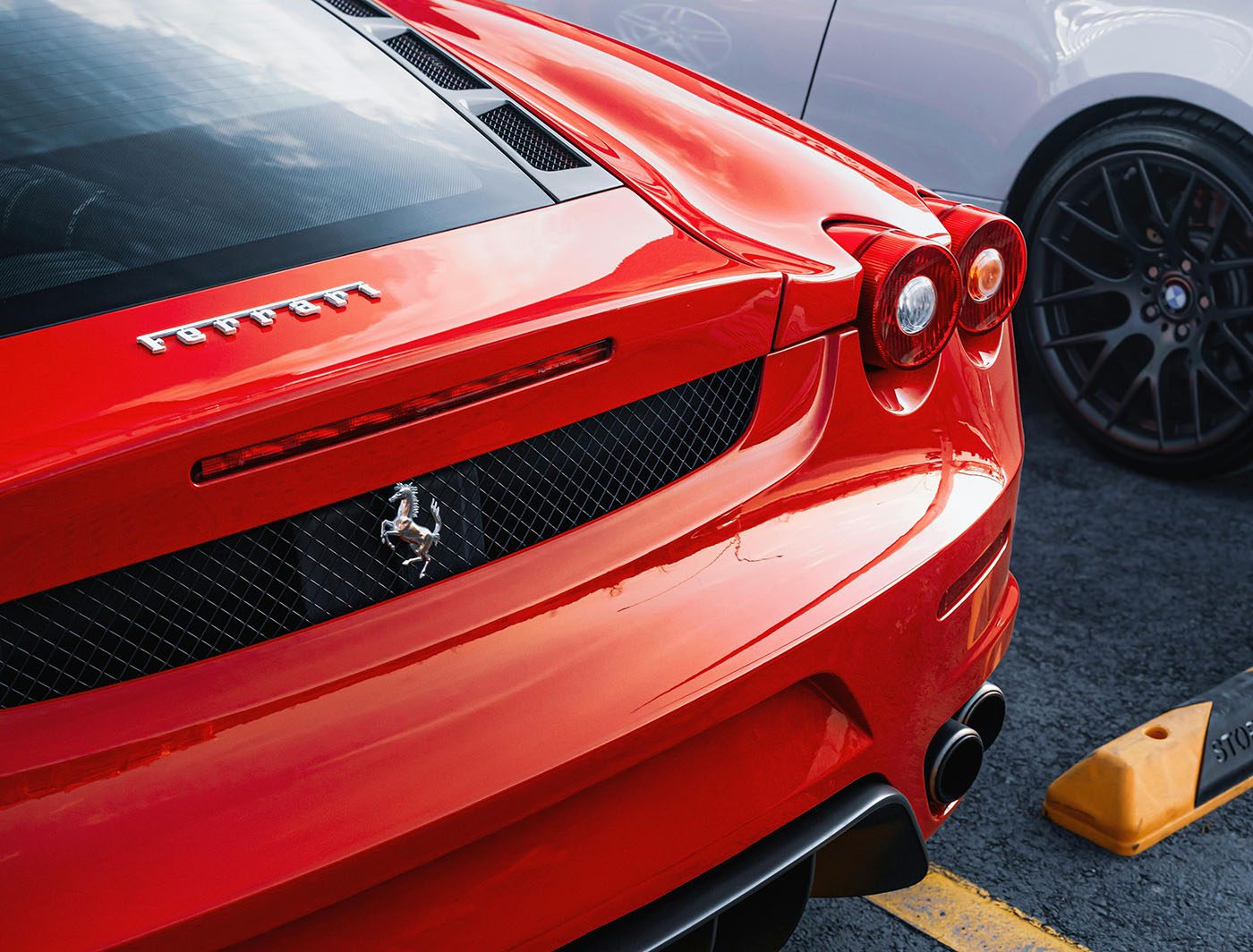 Rear view of a red Ferrari parked next to another car, showcasing its logo, taillights, and exhaust—a perfect candidate for exotic car insurance.