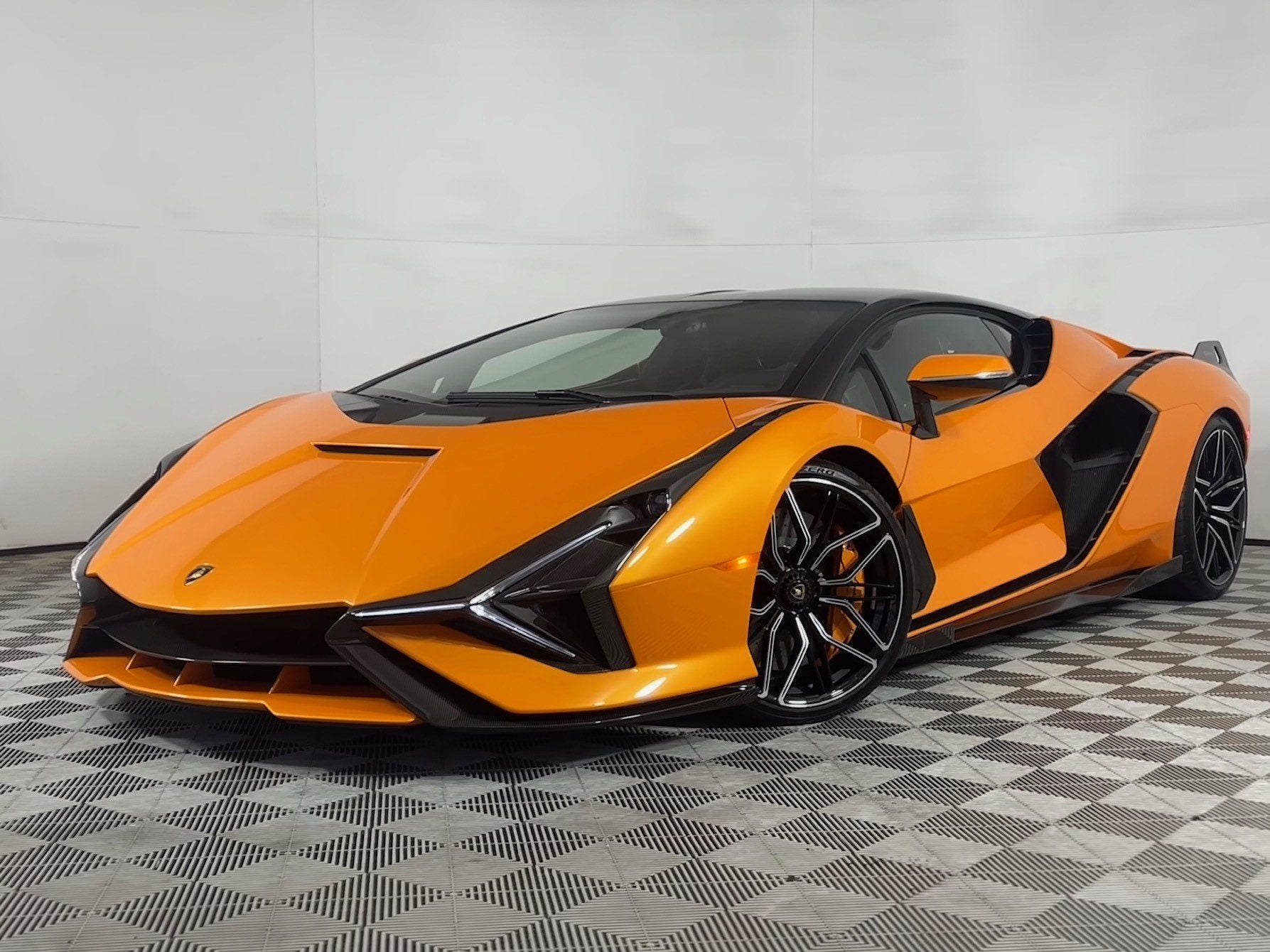 An Arancio Atlas Lamborghini Sián sports car is parked indoors on a patterned floor, viewed from the front left angle, and is now for sale.