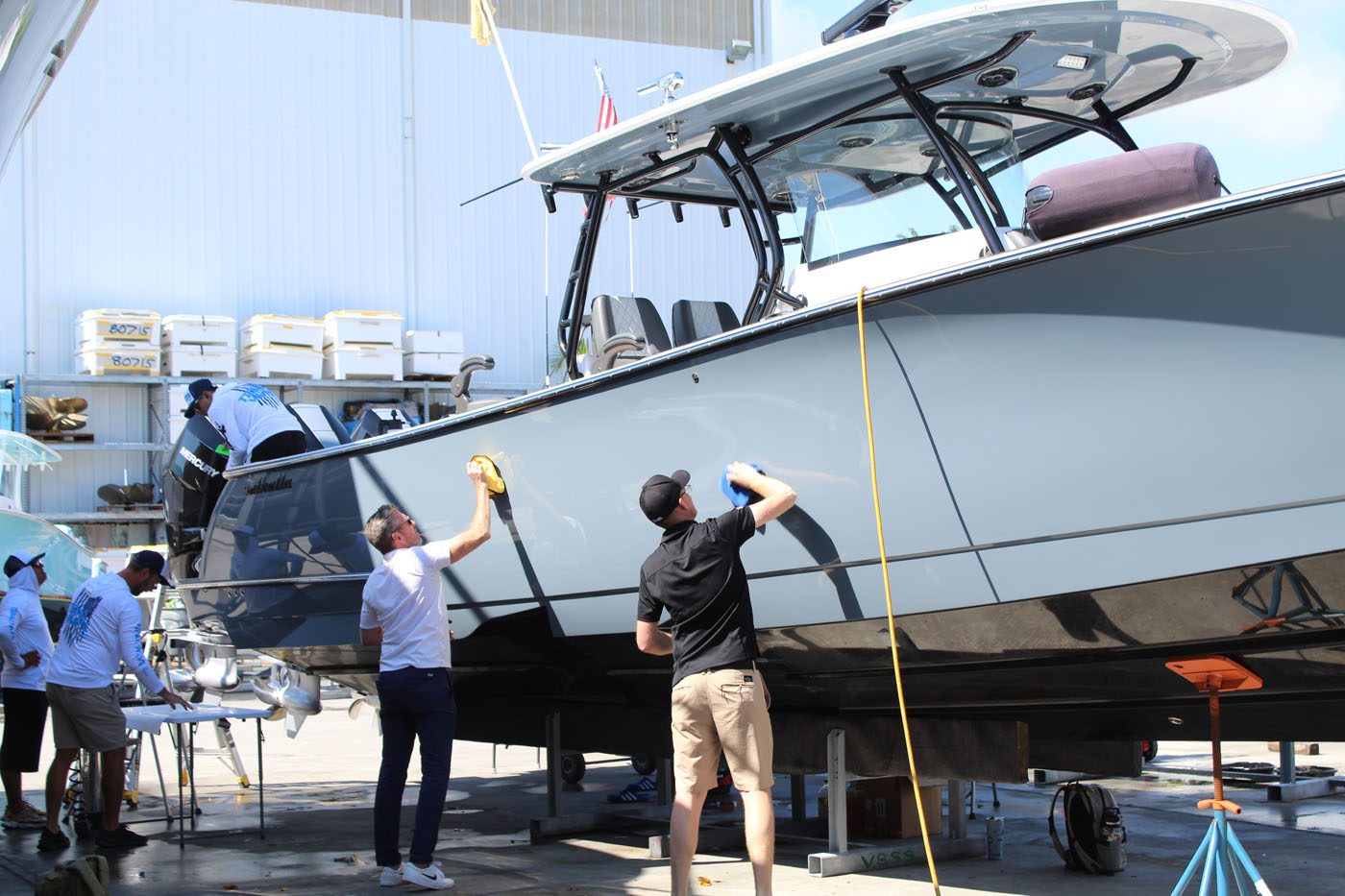 Several people clean and polish a large boat at a dock, with supplies nearby—typical of Florida Boaters who prioritize Marine Protection for their vessels.
