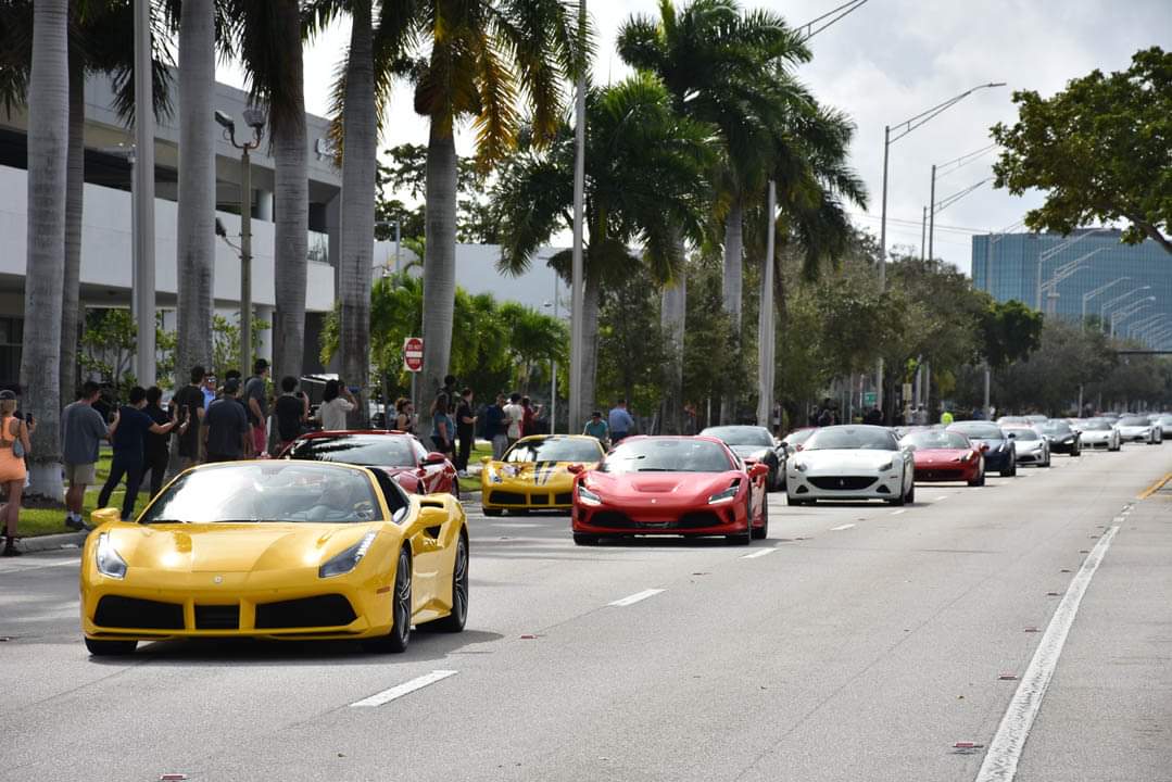 A line of exotic sports cars, including yellow and red ones, speeds down a palm-lined street in South Florida, with eager spectators lining the sidewalk for this thrilling toy rally.