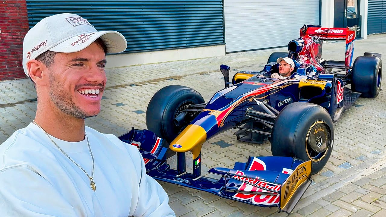 A man in a white shirt and cap grins beside a Red Bull F1 car, dreaming of the Bugatti purchase he'll enjoy on the autobahn.