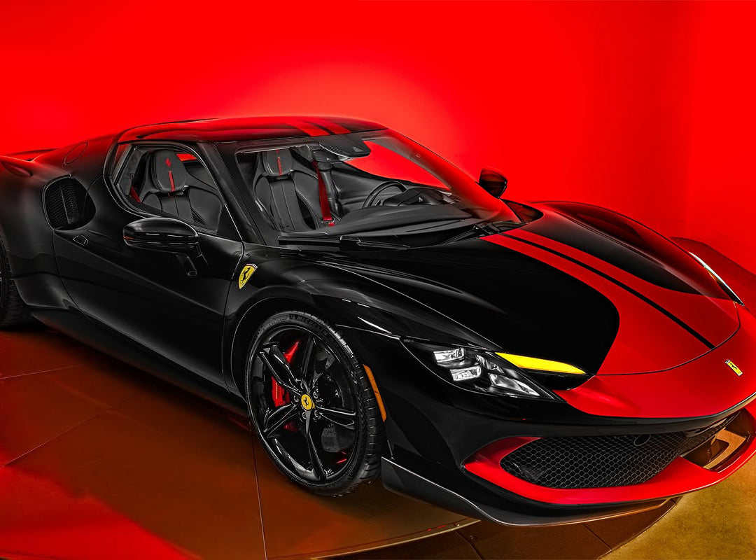 A black Ferrari sports car with yellow accents is displayed under bright red lighting at Ferrari of San Antonio, highlighting its sleek and aerodynamic Italian supercar design.