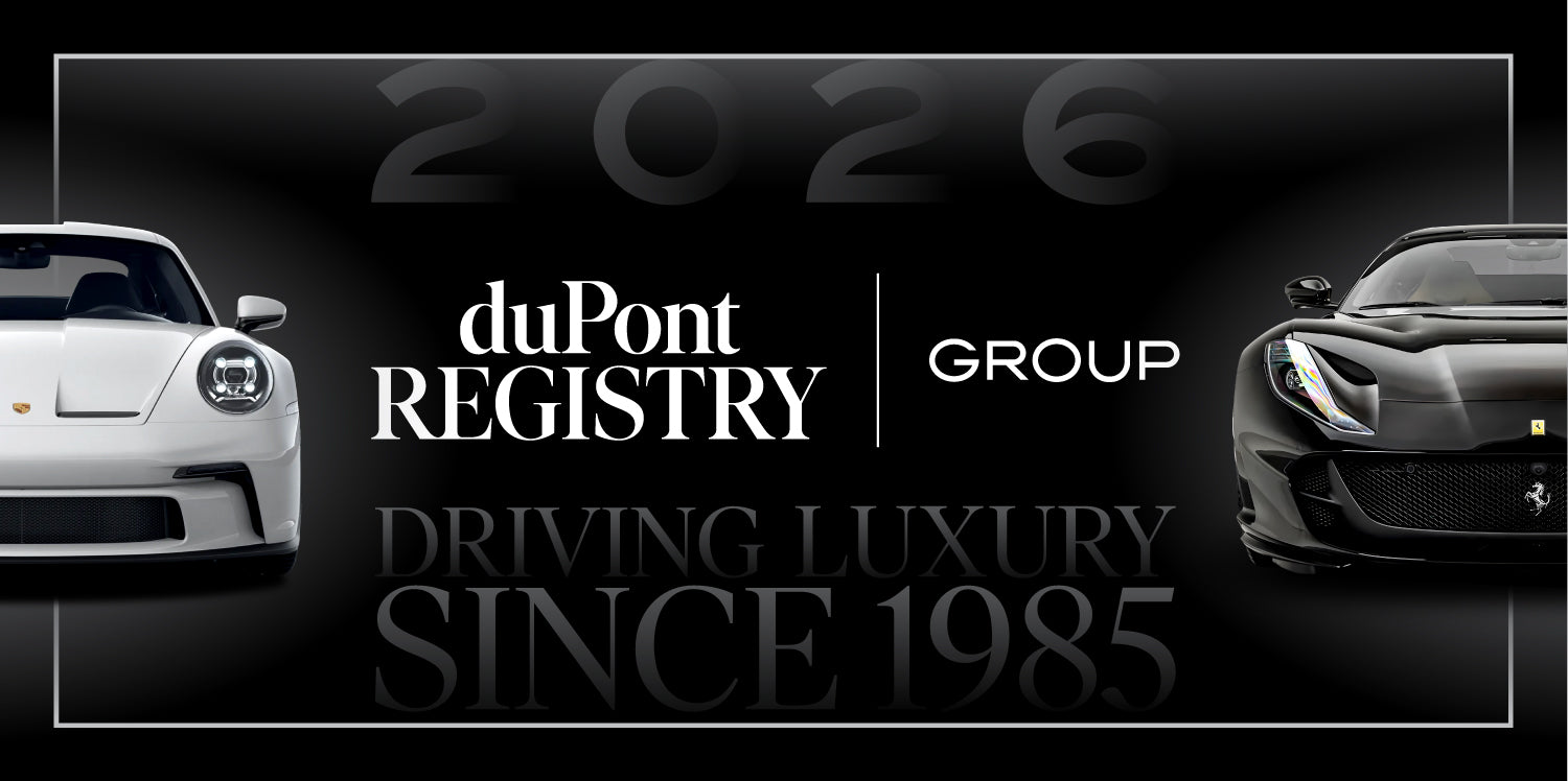 A white Porsche and a black Ferrari flank the duPont REGISTRY Group logo, with "Driving Luxury Since 1985," "2026," and a nod to driving into the future in the background.