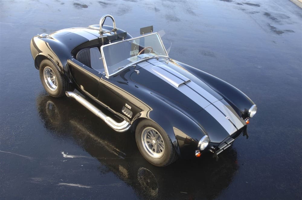 A sleek vintage Shelby 427 Cobra is elegantly parked on a glistening wet surface.