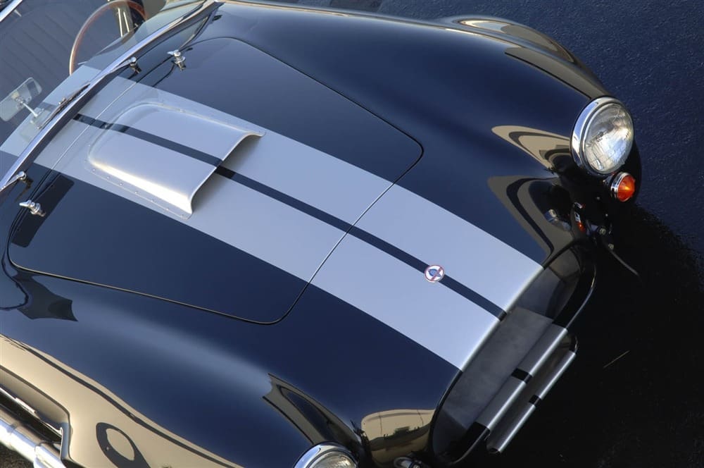 A close-up view of a vintage Shelby 427 Cobra sports car with racing stripes, showcasing its sleek hood and gleaming headlights.