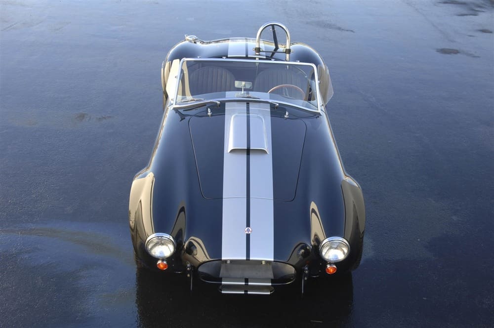 A Shelby 427 Cobra convertible with stripes is elegantly parked on a wet surface.