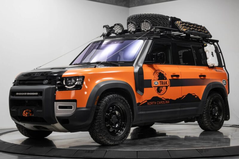 Orange and black off-road SUV with roof rack, extra lights, and Trek North Carolina branding displayed in the showroom—a top choice for those looking to buy Land Rover or discover the best Land Rover Defenders.