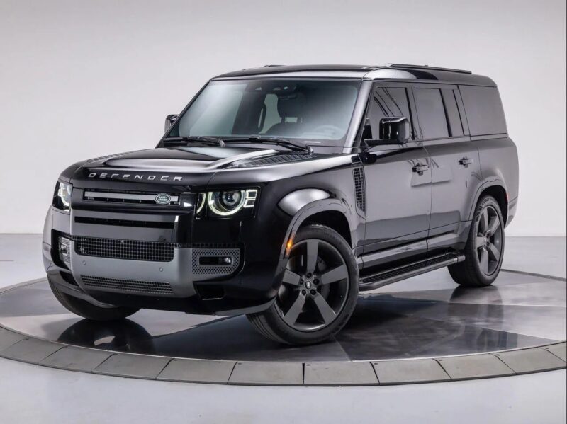 A black Land Rover Defender SUV is parked on a circular platform in a studio with a plain white background, showcasing why many consider it the best Land Rover for both style and performance.