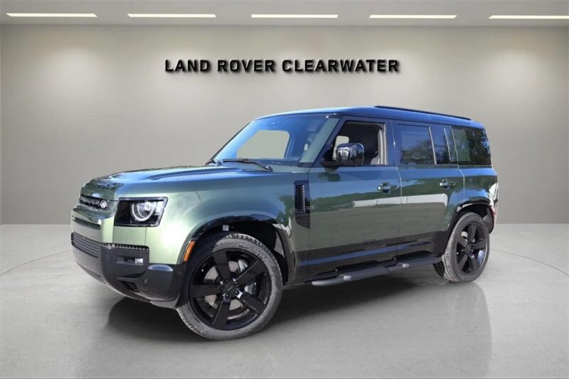 A green Land Rover Defender SUV is parked indoors under the sign "Land Rover Clearwater," showcasing why many choose to buy Land Rover for exceptional quality and performance.