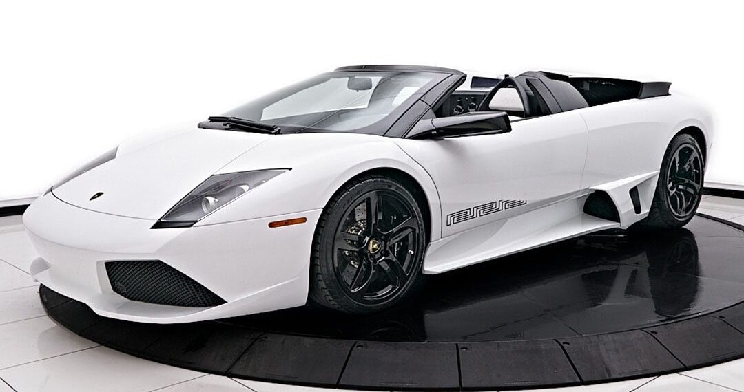 A sleek white Lamborghini Murcielago convertible with black rims is showcased elegantly on a circular platform in the showroom, exuding luxury and style.